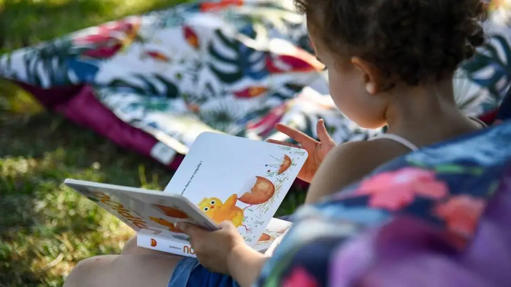 Enfant assise sur l'herbe, lisant un livre d'images
