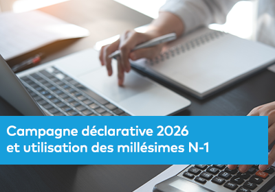 Gros plan d’une personne utilisant un ordinateur portable, avec un carnet de notes et une calculatrice sur le bureau.