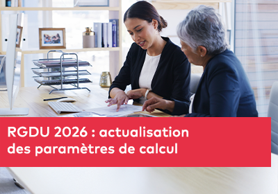 Deux femmes assises à un bureau analysant des documents papier ensemble dans un environnement de bureau lumineux et professionnel.