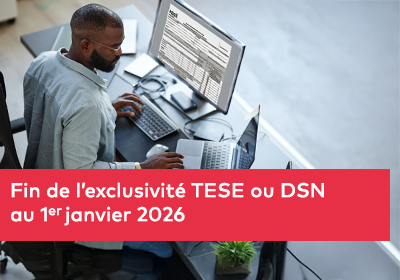 Un homme travaille à un bureau sur un ordinateur et un ordinateur portable, avec un tableau de données affiché à l’écran.