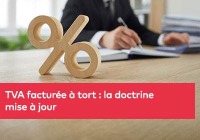 Gros plan sur un signe en bois représentant un pourcentage, symbolisant la TVA, avec un homme calculant en arrière-plan
