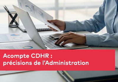 Une personne travaille sur un ordinateur portable tout en tenant des documents imprimés comportant des graphiques et tableaux financiers.